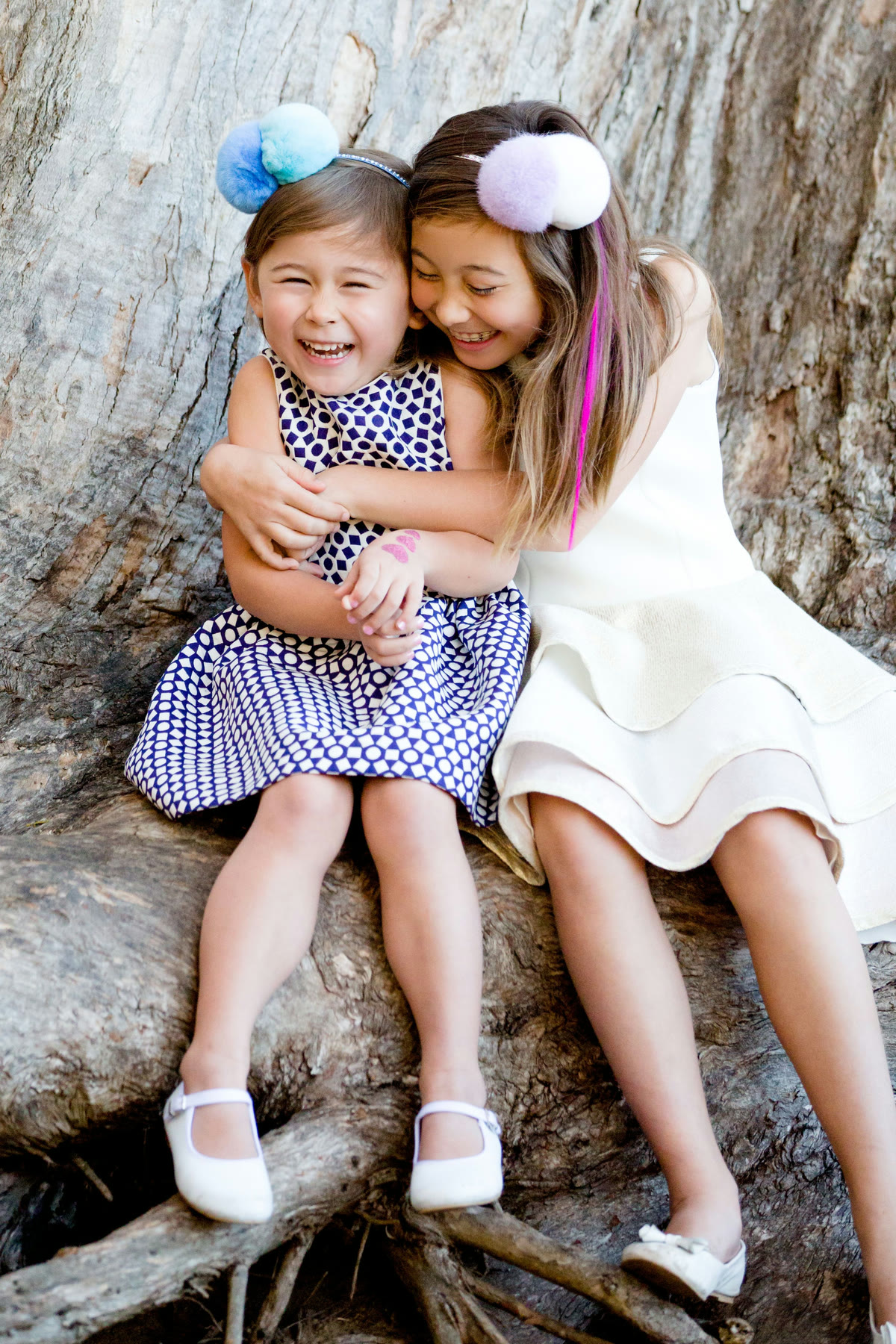 Two young girls laughing together, sitting on a tree trunk
