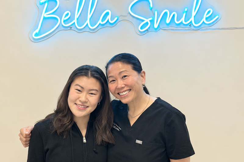 A smiling patient with a Bella Smile team member under the practice’s neon sign